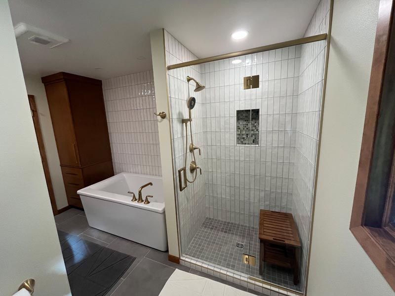 Bathroom with glass shower, white tub, and wood bench on a tiled floor