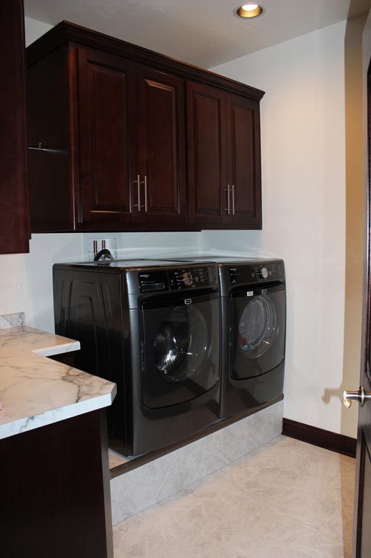 Laundry room with dark cabinets, countertop, and a black washer and dryer against a beige wall.