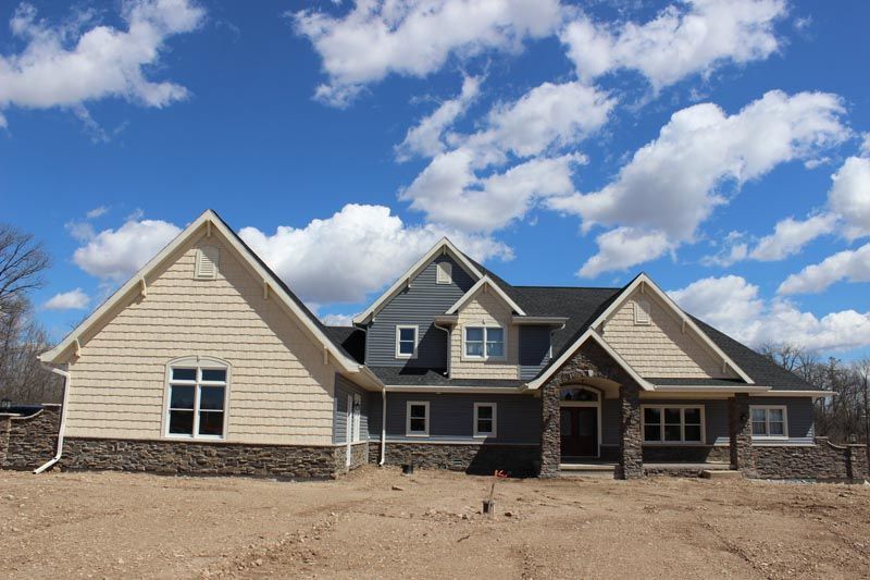 Large beige suburban house under construction with dark roof and blue sky with clouds