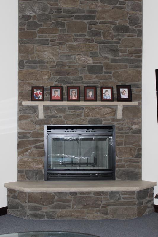 Stone fireplace with mantel, family photos, and a glass-front insert in a living room.