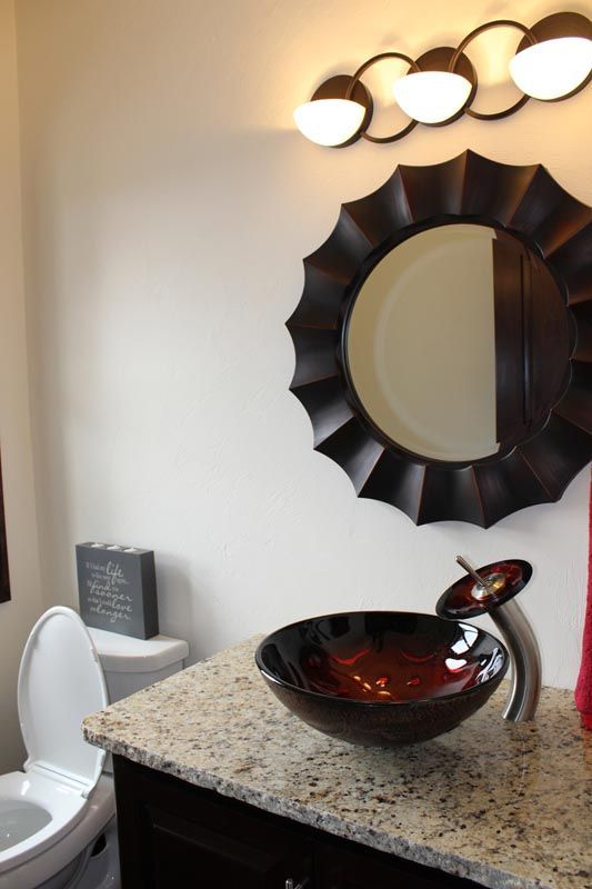 Bathroom vanity with speckled countertop, vessel sink, round mirror, and three-light wall fixture
