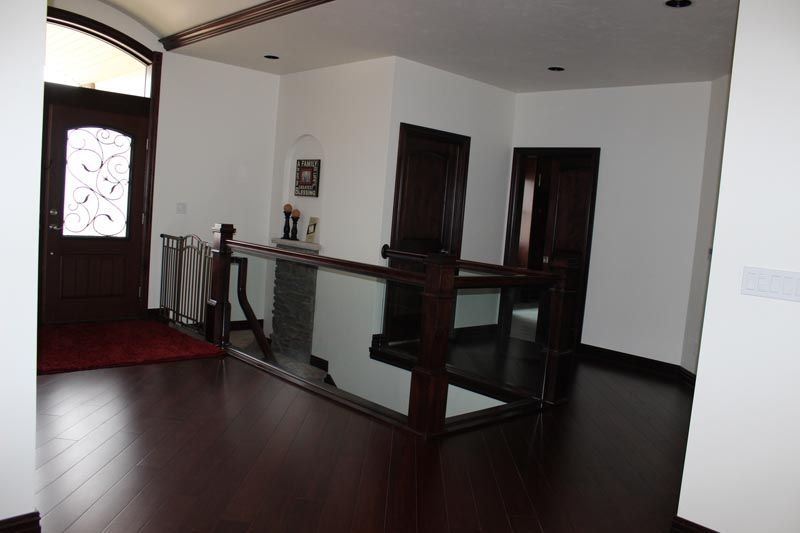 Modern interior hallway with dark wood floors, white walls, and a wooden railing by a front door