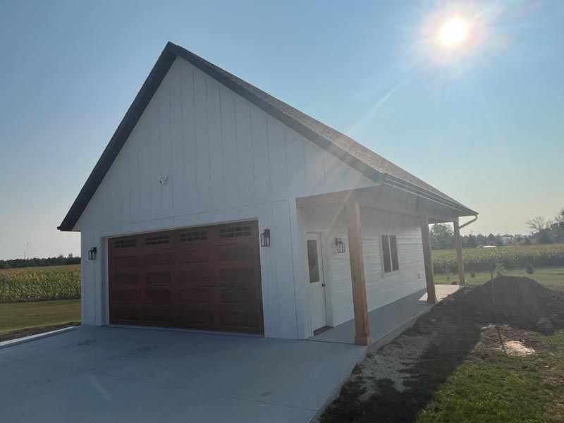 White garage with brown doors and a covered porch on a sunny rural lot