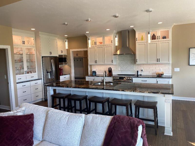 Bright open kitchen with white cabinets, gray island, bar stools, and stainless-steel appliances, seen from a living room