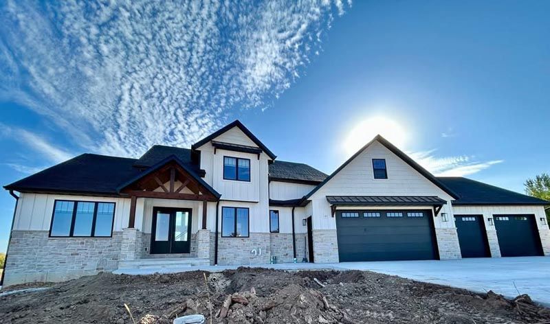 Large modern house under construction with blue roof, white siding, and a partly cloudy sky