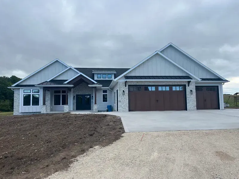 New single-story house with gray siding, brown garage doors, and a driveway under cloudy skies