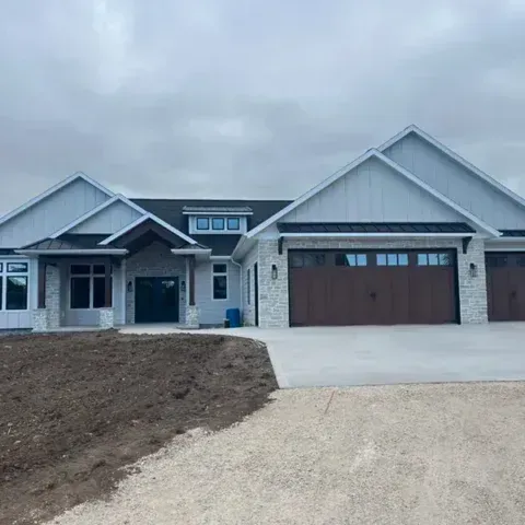New gray house with brown garage door and gravel driveway under cloudy sky