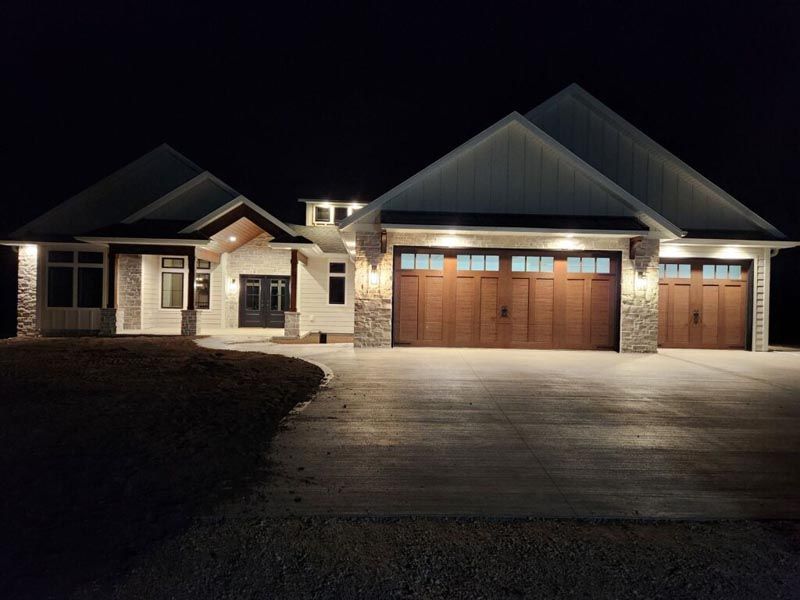 Nighttime view of a house with lit windows, a large wooden garage, and a driveway