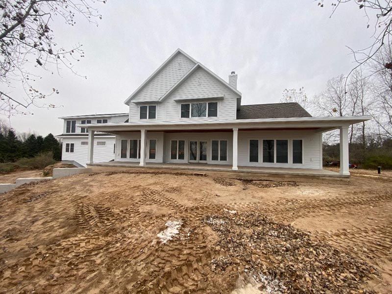 New white house under construction with a covered front porch and bare dirt lot in front