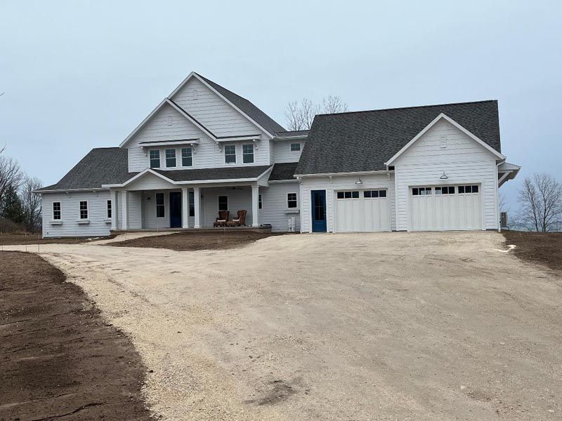 Large white suburban house with a three-car garage on a gravel driveway under an overcast sky