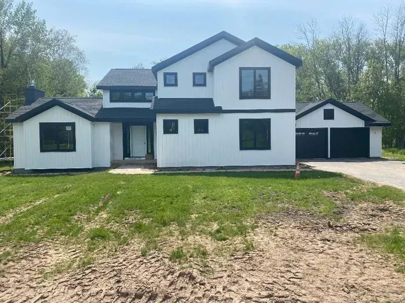 White two-story house with black trim, attached garage, and dirt driveway in a grassy yard