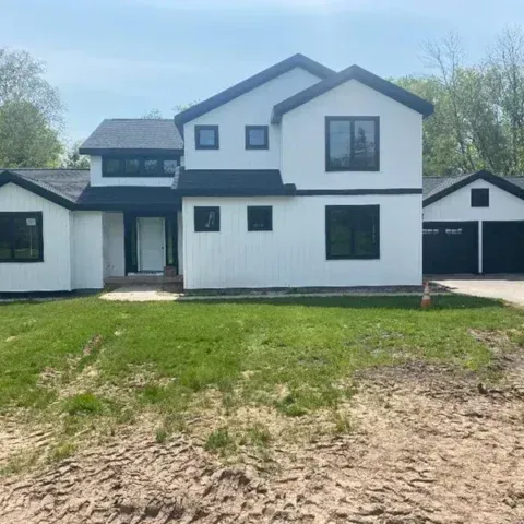 White two-story house with black trim, front lawn, and attached garage under a clear sky
