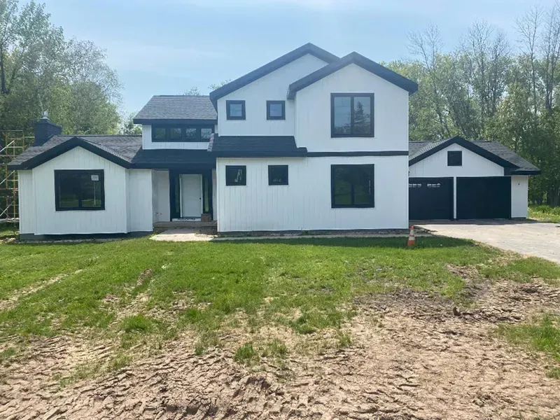 White two-story house with attached garage and dirt driveway under a clear sky