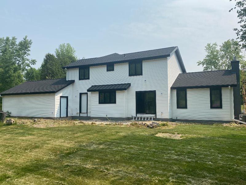 White two-story house with attached garage and small black-roofed wing on a grassy lot under a cloudy sky