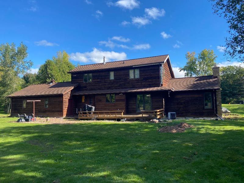 Rustic wooden cabin with a red roof and large lawn under a bright blue sky