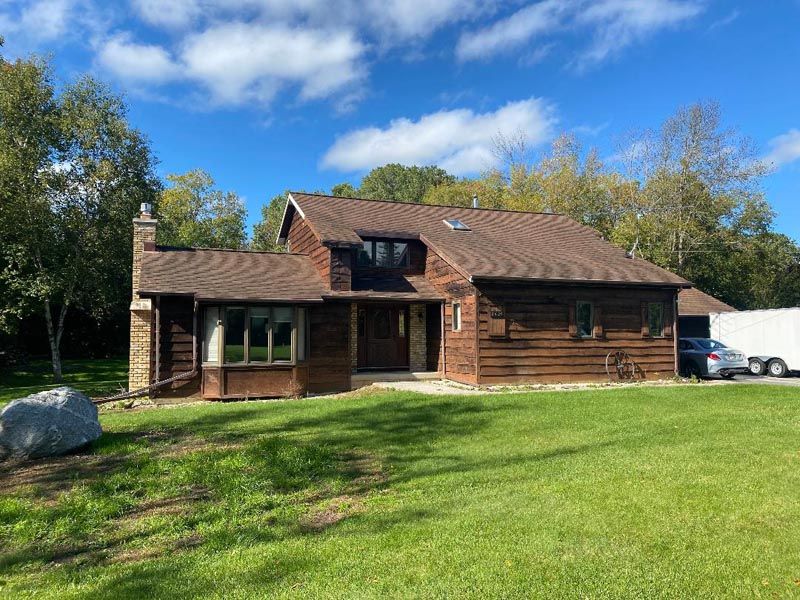 Rustic wooden house with a green lawn, trees, and blue sky with clouds