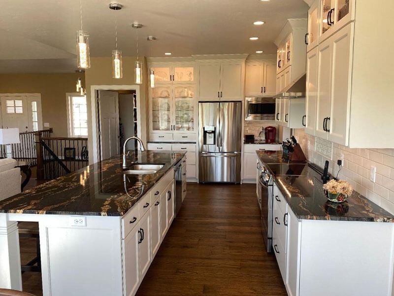 Bright modern kitchen with white cabinets, black countertops, island sink, and stainless steel refrigerator