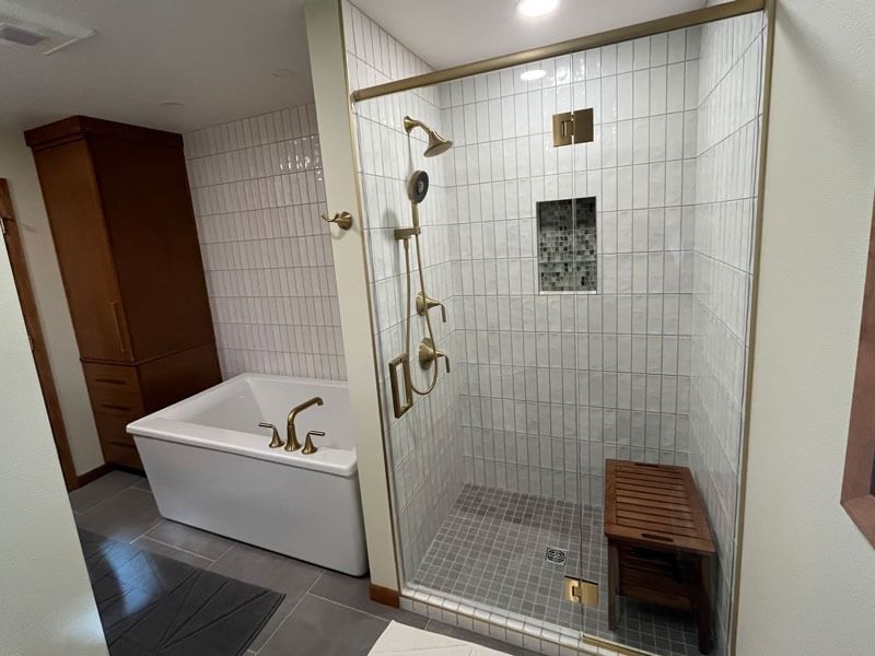 Bathroom with soaking tub and glass-enclosed shower, white tile walls, and a wooden bench.