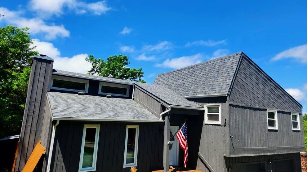 Gray house with a steep roof, American flag by the entrance, under a blue sky