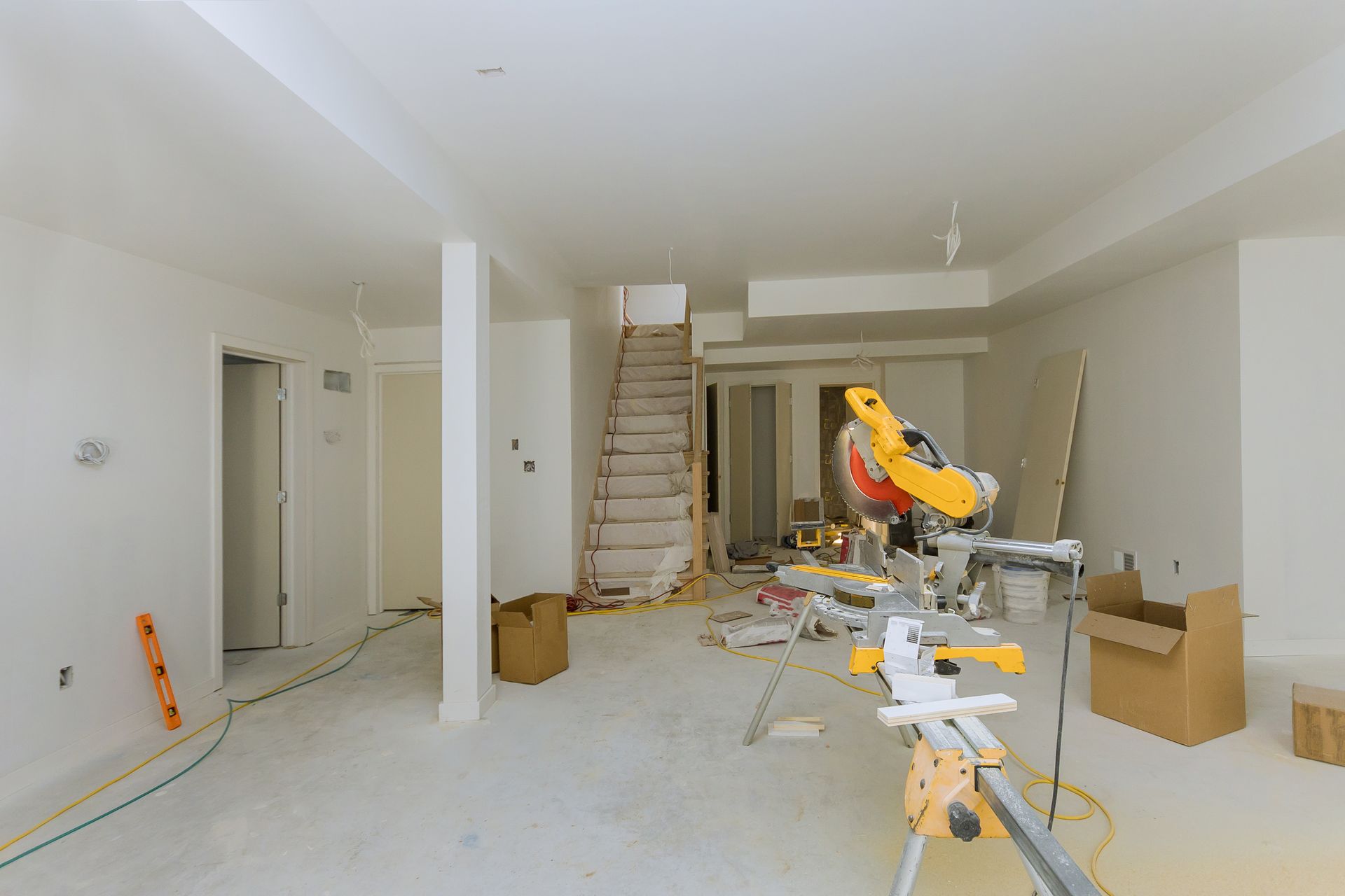 Construction site inside a room with tools, staircase, and a yellow miter saw table