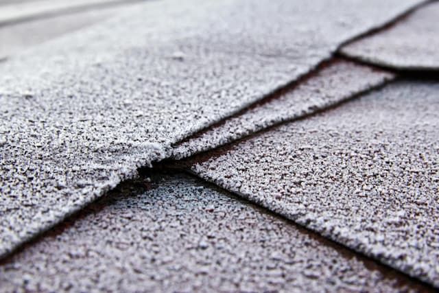 Close-up of overlapping gray asphalt roof shingles with a rough, textured surface