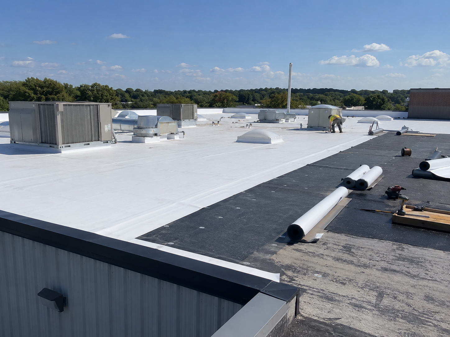 Flat rooftop with white membrane, HVAC units, and construction materials under a clear sky.