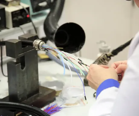 Technician handling multicolored wires attached to a metal connector in a workshop setting