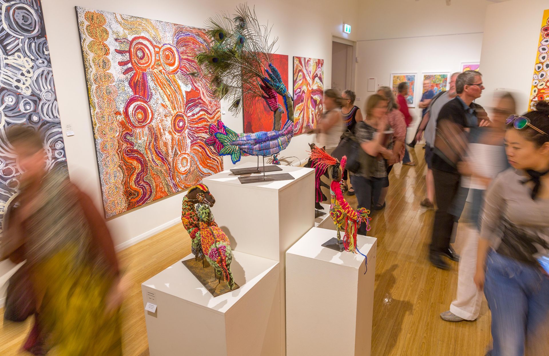 People view vibrant, patterned art and sculptures in a bright, modern gallery space.