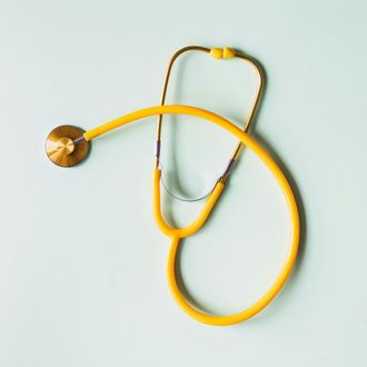 A yellow stethoscope with metallic parts against a light blue background.