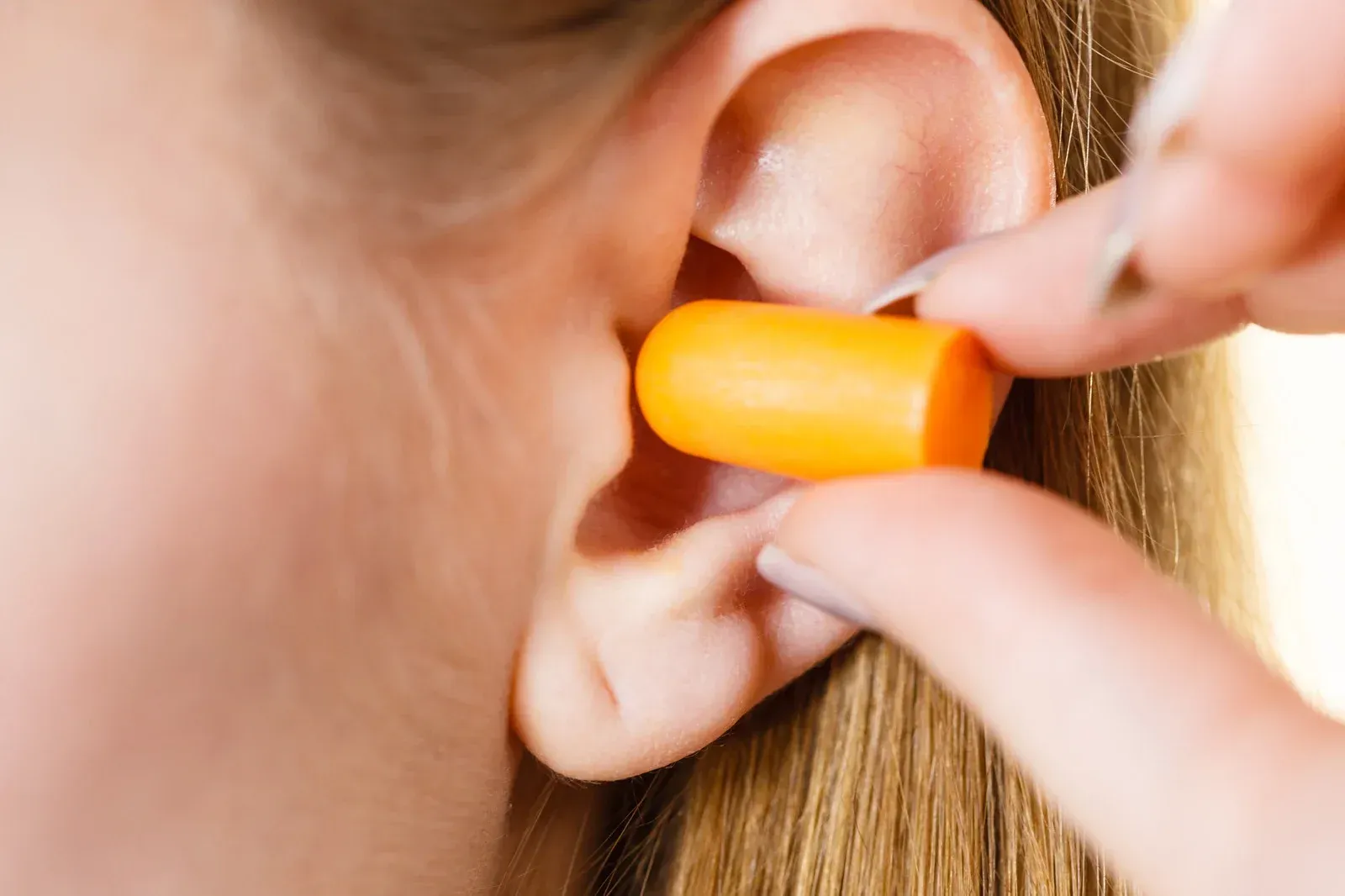 A woman is putting an orange ear plug in her ear.