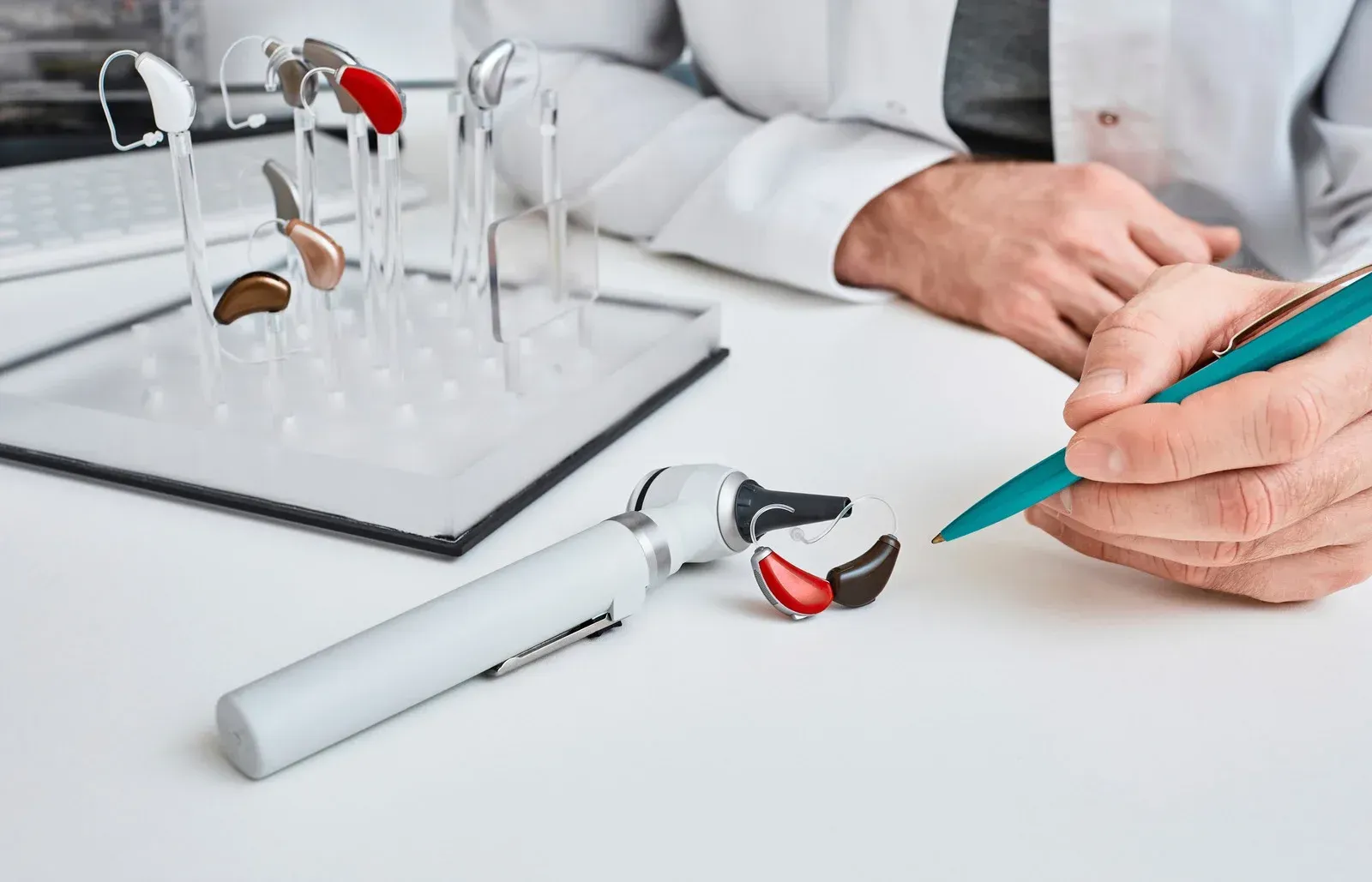 A man is sitting at a table looking at hearing aids and writing on a clipboard.