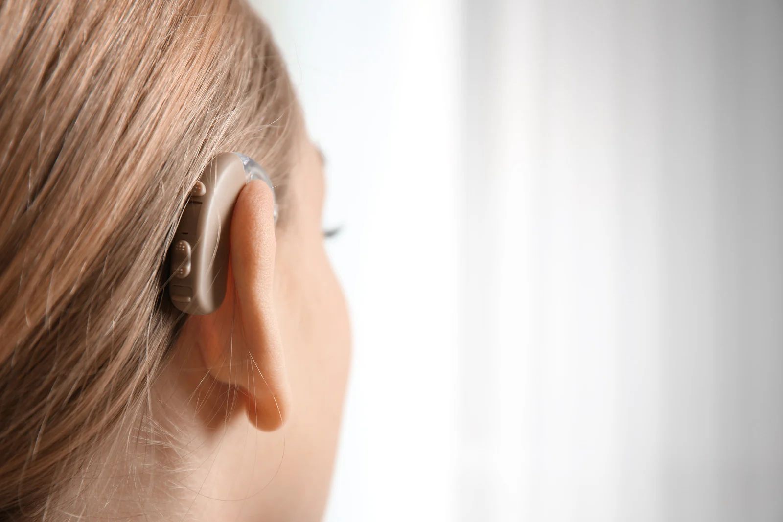 Close-up of a person wearing a behind-the-ear hearing aid against a bright background