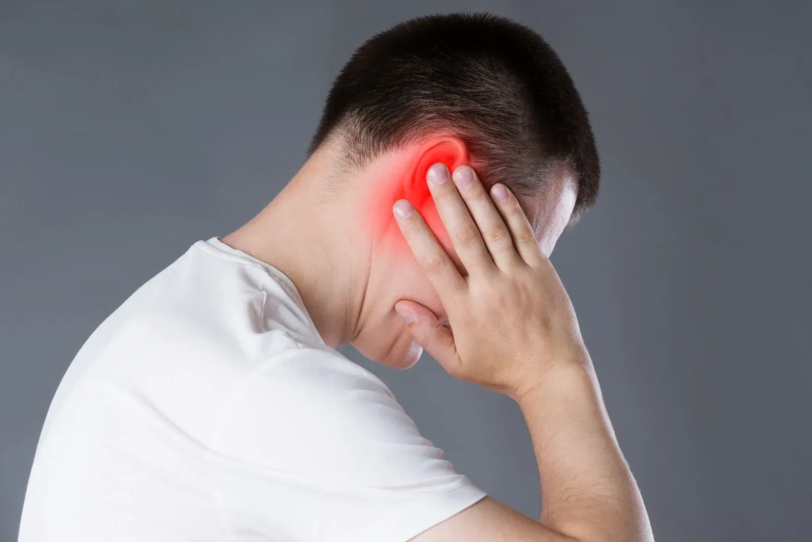 A man is covering his ear with his hand because he has a headache.