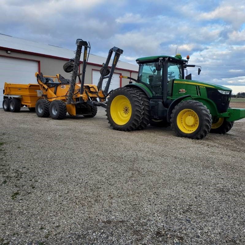 A green and yellow tractor is parked next to a yellow trailer.