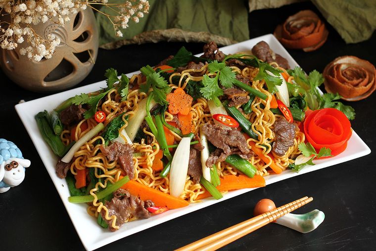 Bowl of Vietnamese noodle soup with shrimp, herbs, lime, and chilies on a dark background