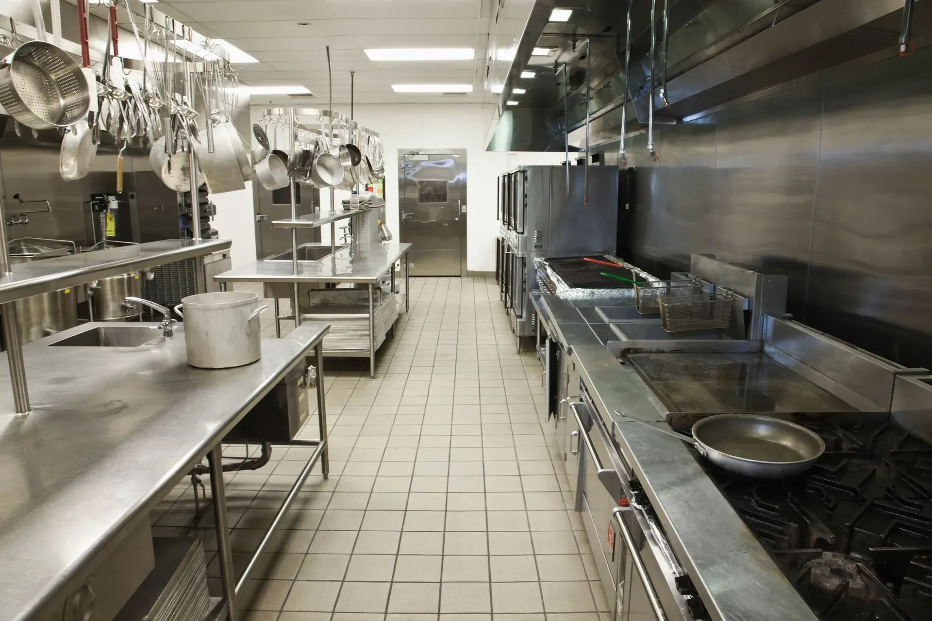 An empty kitchen with stainless steel appliances and pots and pans hanging from the ceiling An empty kitchen with stainless steel appliances and pots and pans hanging from the ceiling