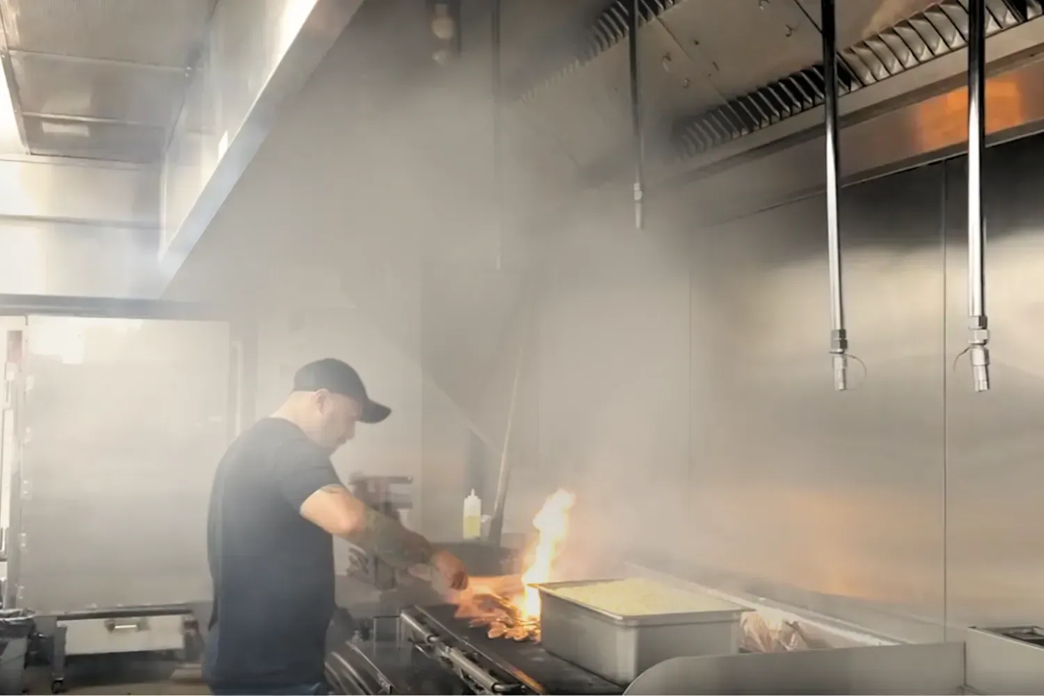 A man is cooking food on a grill in a kitchen. A man is cooking food on a grill in a kitchen.