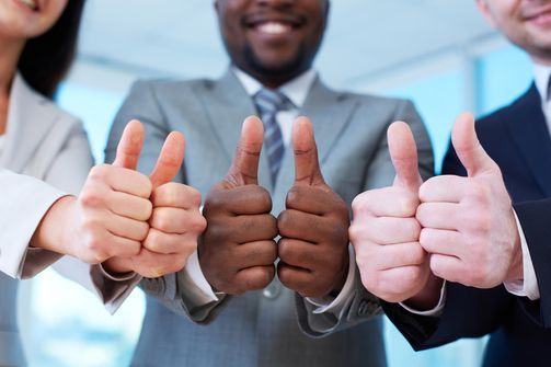 Three business professionals in suits smile while giving a thumbs-up gesture toward the camera.