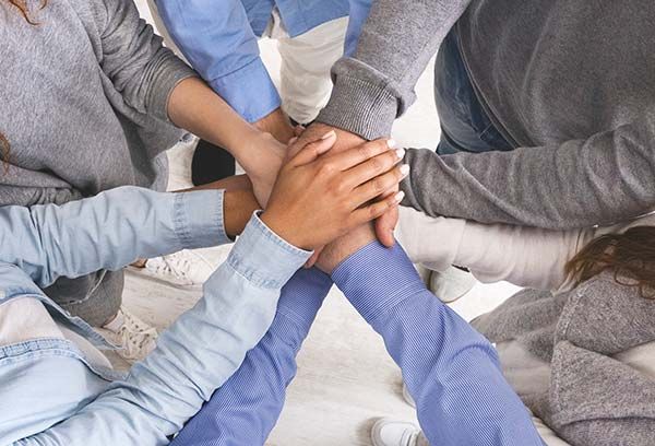 A group of people standing in a circle, placing their hands on top of each other in a gesture of unity and teamwork.