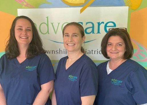 Three women are posing for a picture in front of a sign that says Advocare.