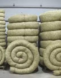 Stacks of rolled beige blankets or insulation bales arranged in a warehouse-like setting.