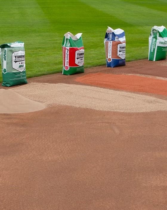 Four small painted containers on a baseball field near the infield dirt and grass line.