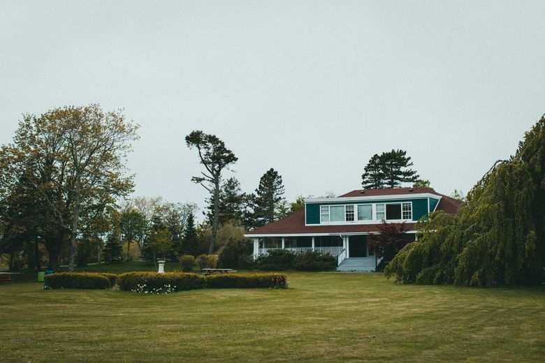 Red house with white trim on a large grassy lawn under an overcast sky