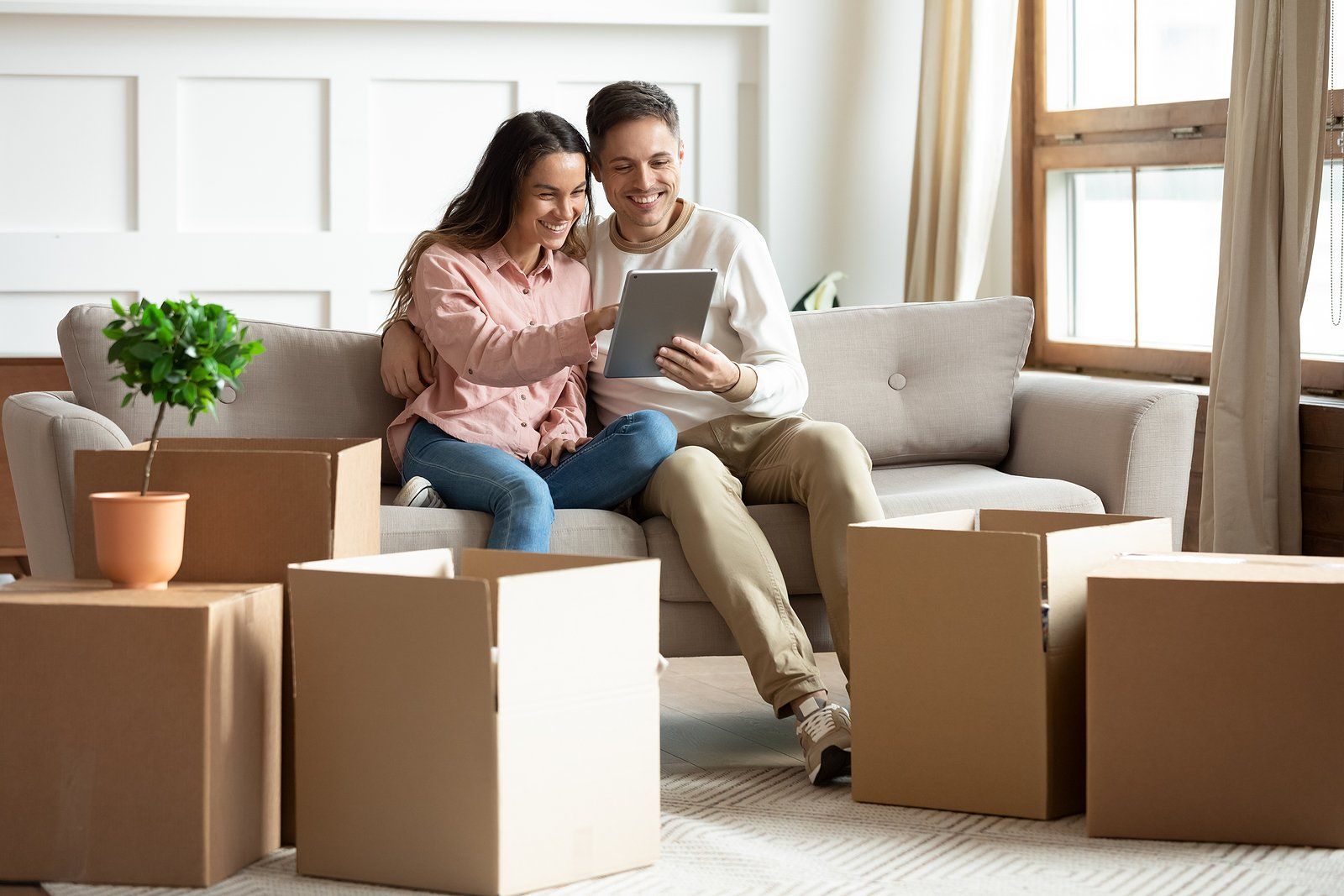 Two people sitting on a couch reviewing documents, surrounded by moving boxes in a bright living room.