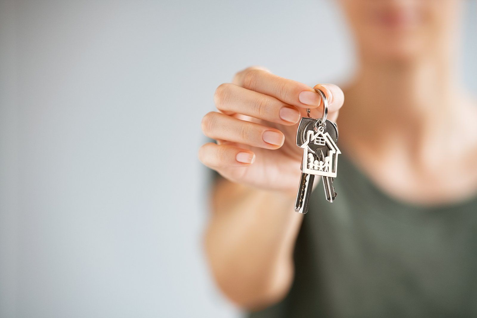 Hand holding a set of keys toward the camera, with a blurred person in the background