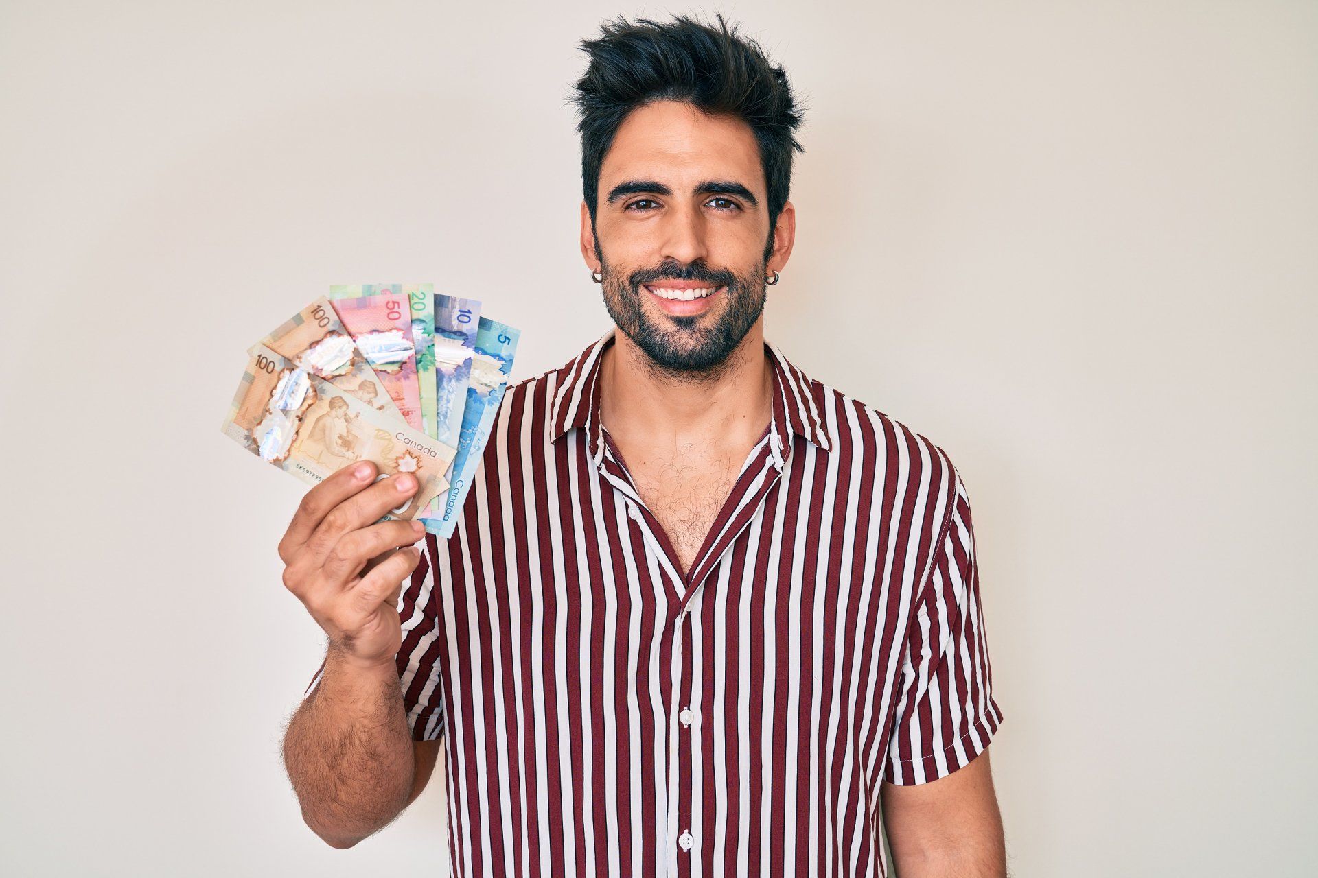 Man smiling and holding a fan of colorful banknotes against a plain background