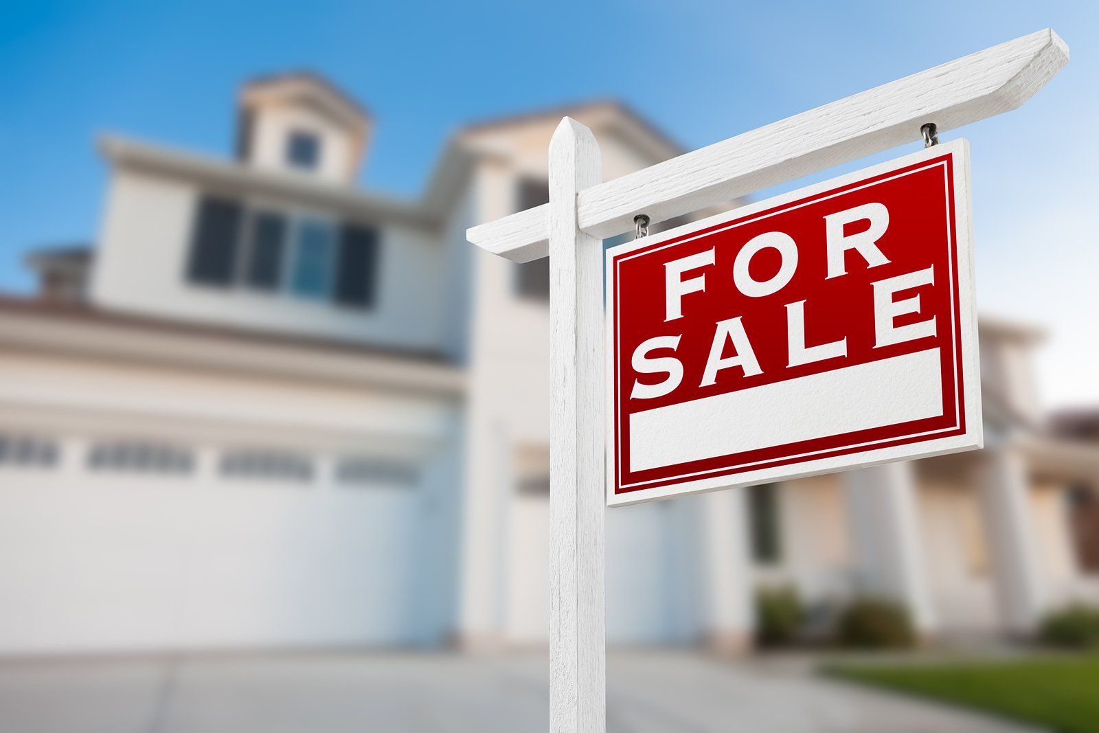 Red “For Sale” sign hanging outside a blurred suburban house