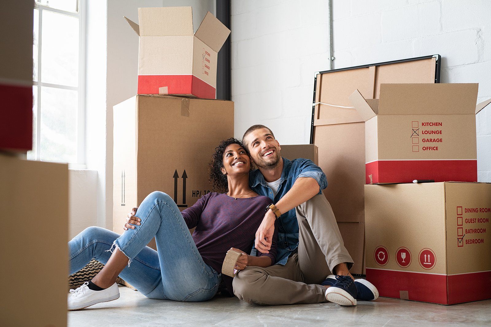 Couple sitting on the floor among moving boxes in a new apartment, smiling and relaxing together.