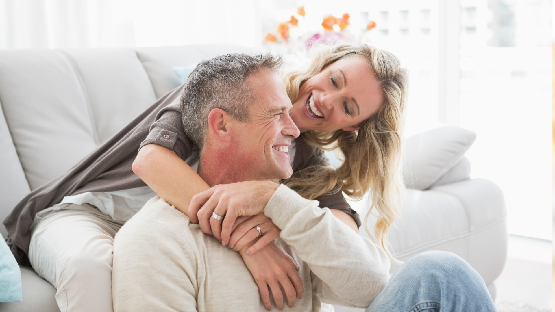 A smiling couple embracing on a white couch in a bright living room.