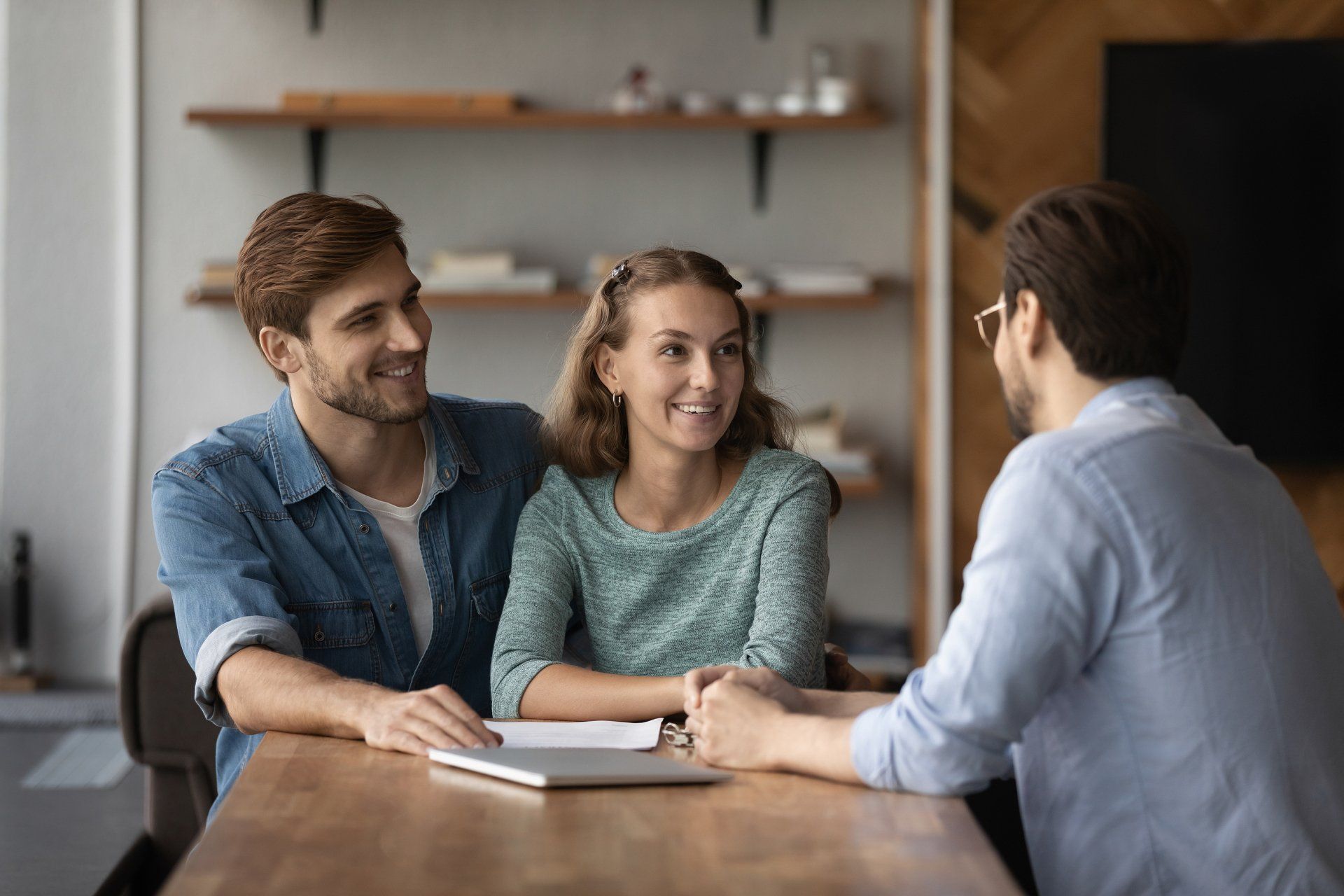 Three people in a meeting at a wooden table, smiling and talking in a modern office